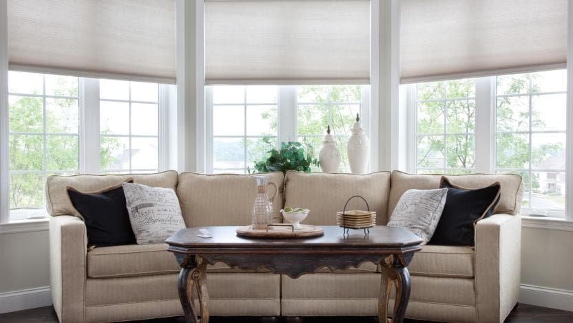 Lutron motorized shades softly lowered across the bay windows of a sunroom overlooking the water.