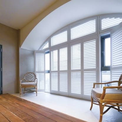 White plantation shutters custom-fit to a tall arched window wall in a sunlit Sarasota room