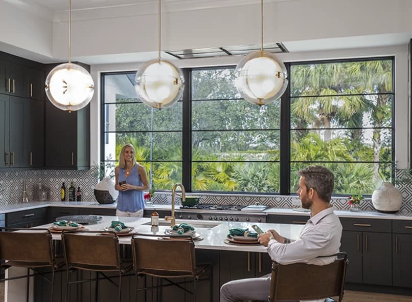 Bright modern kitchen with large black-framed PGT ClassicVue Max aluminum windows overlooking palms and greenery