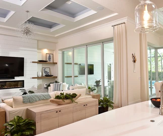 Bright coastal living room with large white-framed PGT sliding glass doors opening to a screened lanai