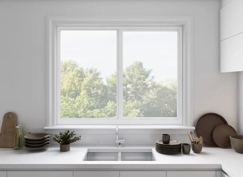 Clean white kitchen with a white-framed PGT Scout aluminum sliding window above the sink looking out to green trees
