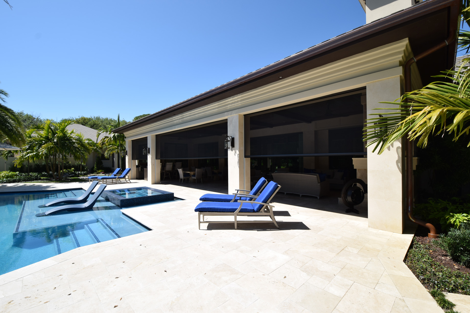 Dark Fenetex One-Track shade screens lowered across a long row of lanai openings on a poolside Florida home with travertine decking and palms