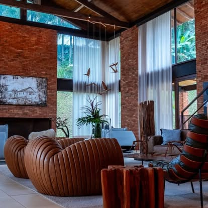 Dramatic double-height brick living room with white sheer drapery on tall windows and leather sofas