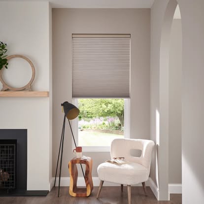 Cozy neutral reading nook with a cellular honeycomb shade on the window, a boucle chair, and a fireplace