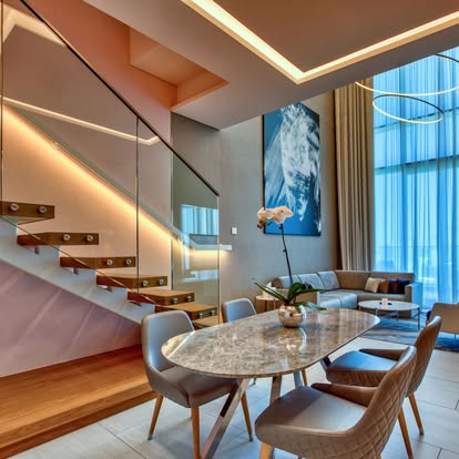 Double-height condo with a floating glass staircase and sheer drapery on tall windows above a marble dining table