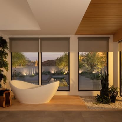 Gray solar roller shades on three large windows in a desert modern bathroom with a freestanding tub