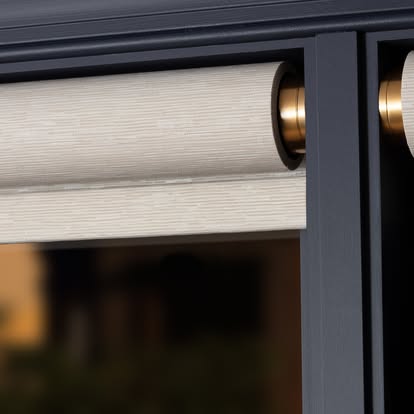 Close-up of a natural roller shade on a brass roller against a deep navy window frame