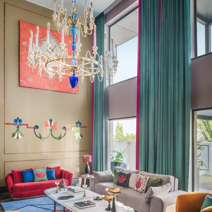 Floor-to-ceiling teal drapery with magenta trim on double-height windows in a dramatic living room