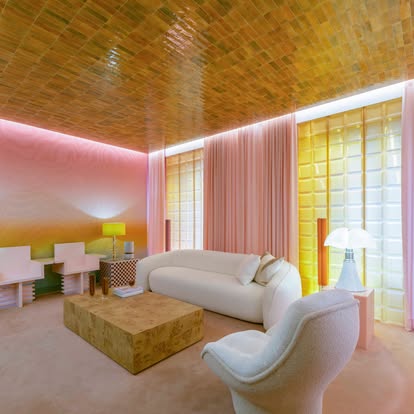 Colorful modern lounge with pink sheer drapery, a glowing yellow glass-block wall, and a tiled ceiling