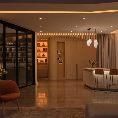 Warmly lit modern lounge and bar area with drapery and layered cove lighting at dusk