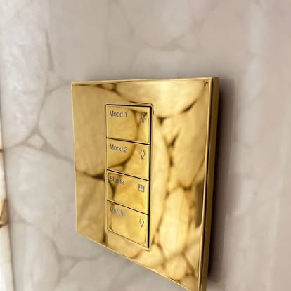 Polished brass Lutron keypad with Mood 1, Mood 2, Shade, and On/Off buttons on a backlit onyx wall