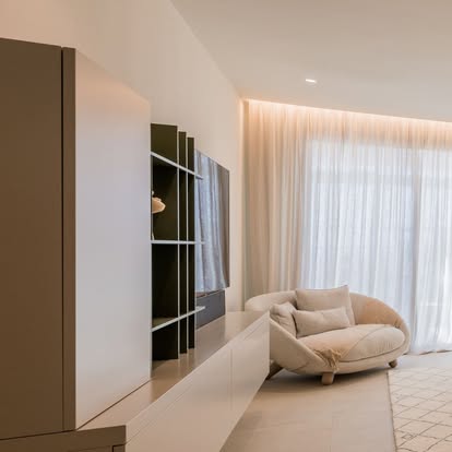 Minimalist living room with sheer drapery drawn across a window wall beside a media wall and boucle chair
