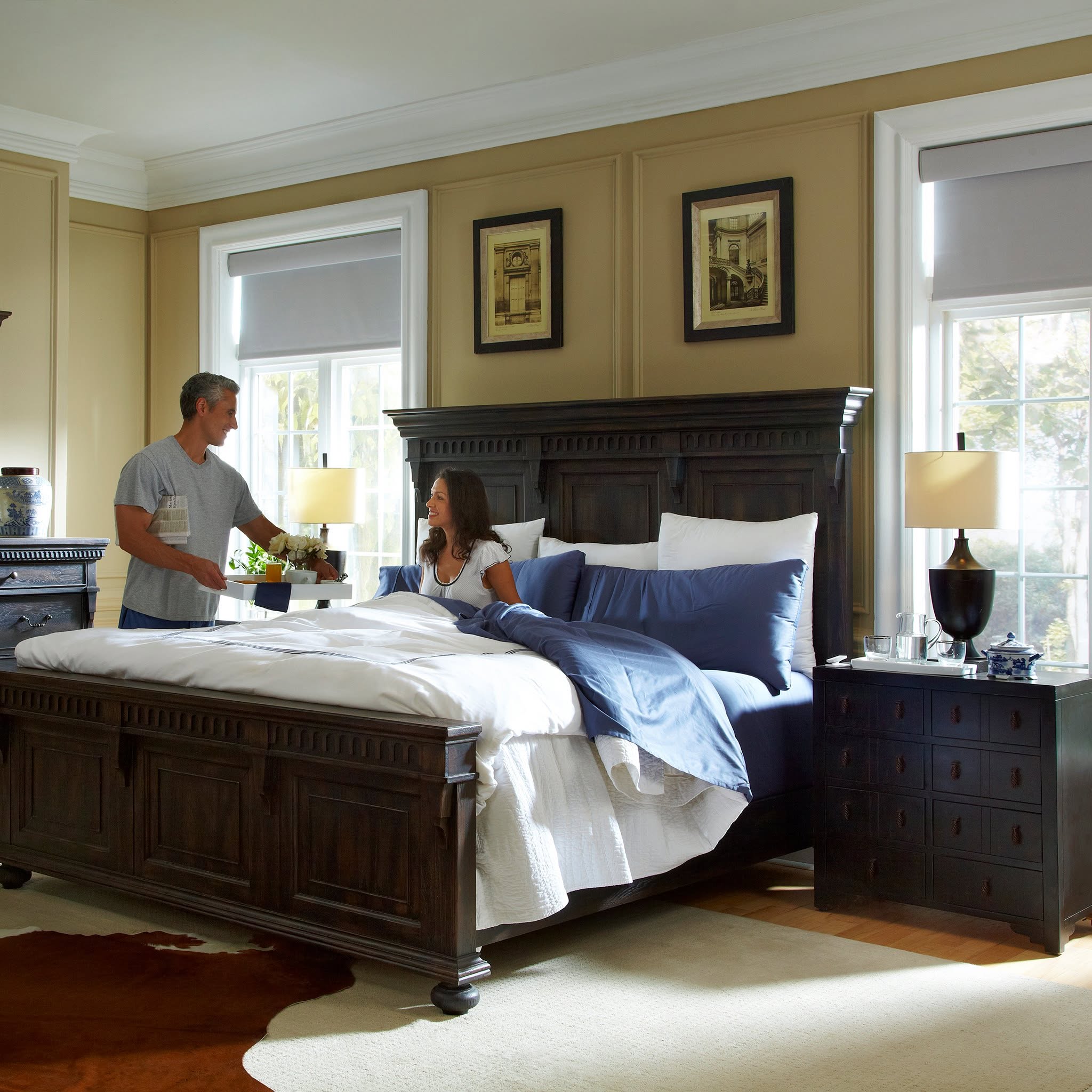 Gray motorized shades lowered across bedroom windows as a couple enjoys breakfast in bed