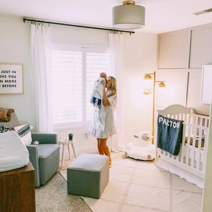 Parent holding a baby in a bright, calm nursery with soft window treatments and layered lighting