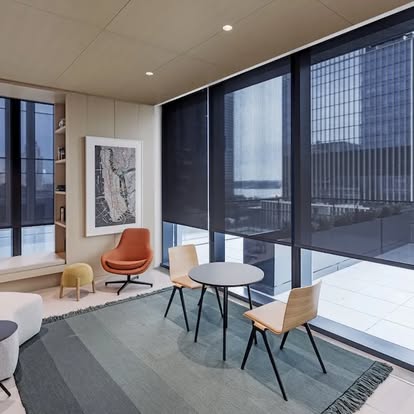 Dark solar roller shades lowered across floor-to-ceiling office windows above a seating area with a city view