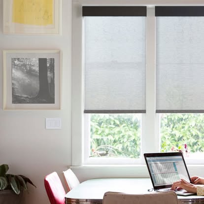 Light gray roller shades over a home-office window with a laptop and framed art
