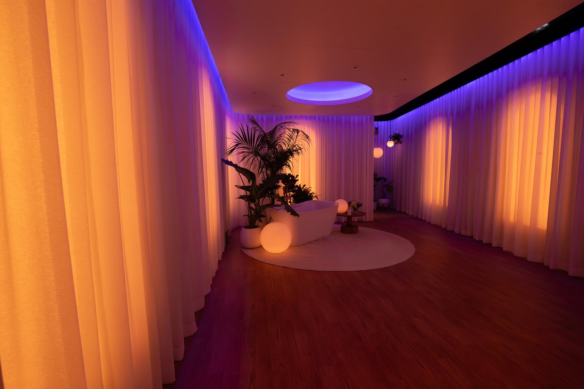 Spa-like room wrapped in floor-to-ceiling sheer drapery lit in warm and cool tones around a freestanding tub