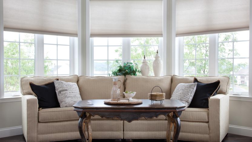 Lutron motorized shades softly lowered across the bay windows of a sunroom overlooking the water.