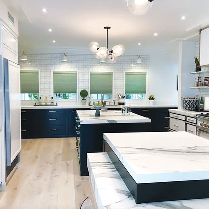 Green cellular honeycomb shades on a row of windows in a modern navy kitchen with marble islands