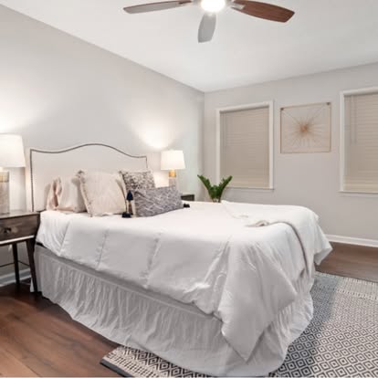 White faux wood blinds on two windows in a neutral staged bedroom with a ceiling fan