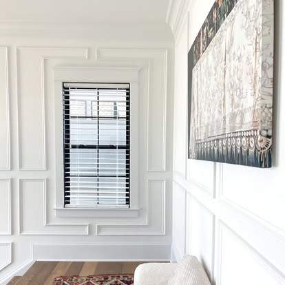 White faux wood blinds in a wainscoted room with paneled walls and framed art