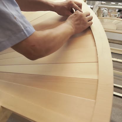A craftsman hand-finishing a curved wooden shutter panel in the Norman workshop