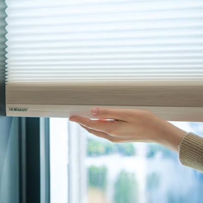 Close-up of a hand adjusting a cordless Norman honeycomb shade showing its pleated cells