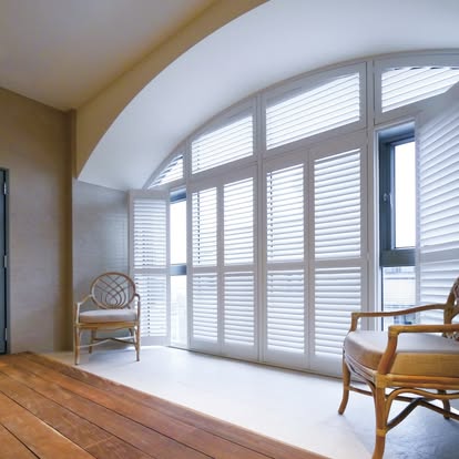 White plantation shutters custom-fit to a tall arched window wall in a sunlit room