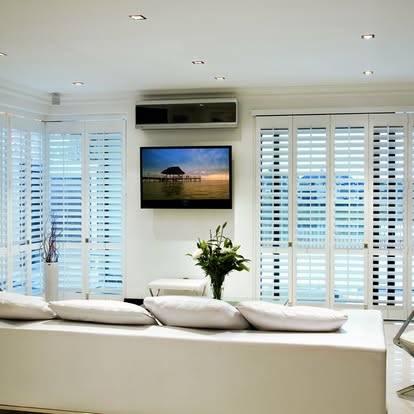 White plantation shutters flanking a wall-mounted TV across a crisp white living room