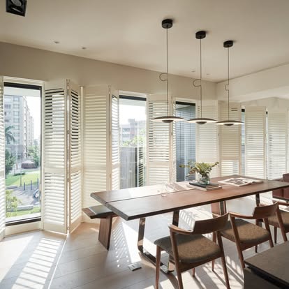 Bi-fold track plantation shutters folding open across a dining room with a city view