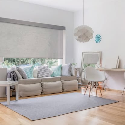 Textured gray roller shade lowered over a wide living room window with a low sectional