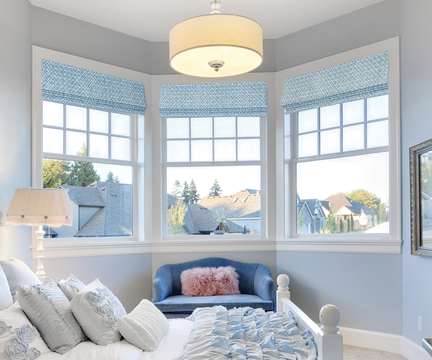 Three blue geometric-print Roman shades on a coastal bedroom bay window with a drum pendant