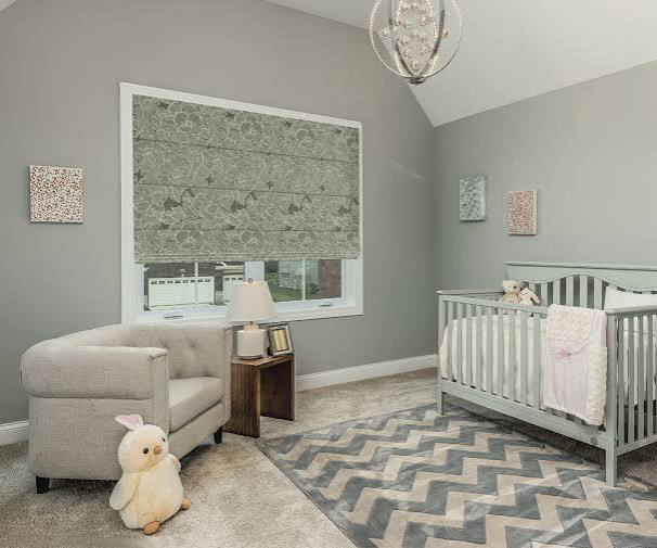 Soft gray-green botanical-print Roman shade over a nursery window beside a gray crib