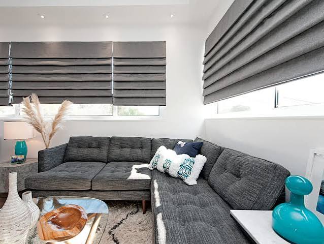 Charcoal hobbled-fold Roman shades over two windows in a modern living room with a dark sectional