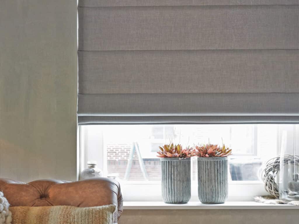 Close-up of a greige Belgian linen Roman shade in soft hobbled folds above a windowsill