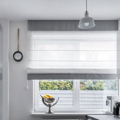 White Roman shade with a gray banded valance over a kitchen window with a pendant light