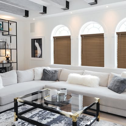 Warm wood blinds on arched windows in a bright white living room with a low sectional