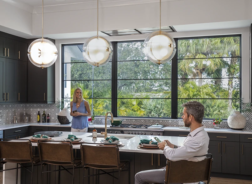 Bright modern kitchen with large black-framed PGT ClassicVue Max aluminum windows overlooking palms and greenery