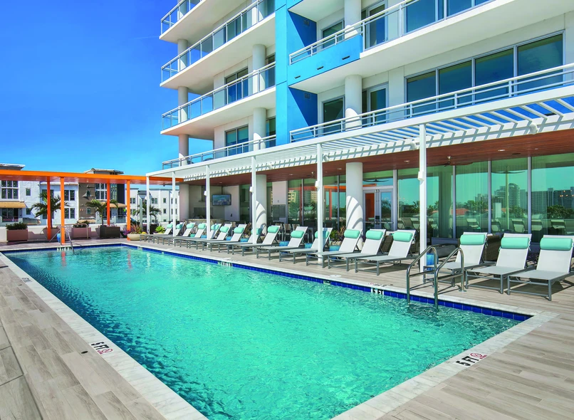 Modern multi-story building with a rooftop resort-style pool and expansive PGT Commercial aluminum windows and glass doors
