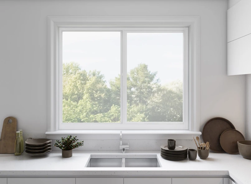 Clean white kitchen with a white-framed PGT Scout aluminum sliding window above the sink looking out to green trees