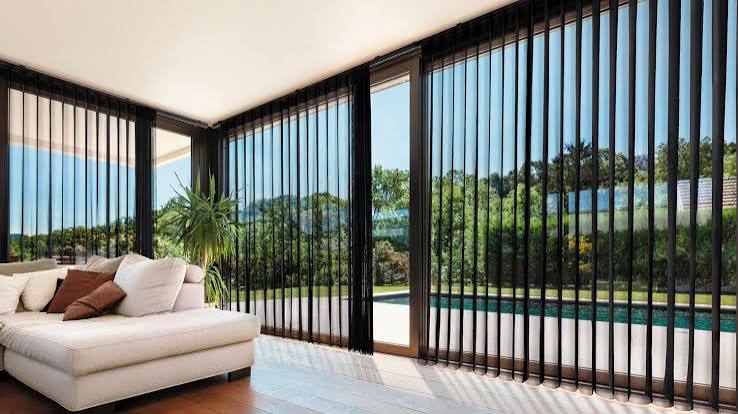 Large sliding glass doors dressed with roller shades and drapery in a bright Florida living room