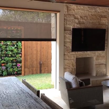 Motorized exterior solar screen lowered over a covered patio opening beside a stone fireplace
