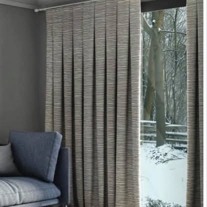 Sliding panel-track shades in a natural woven texture beside a gray armchair — product style example