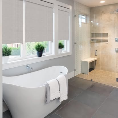 Bright bathroom with light woven roller shades above a freestanding tub — product style example