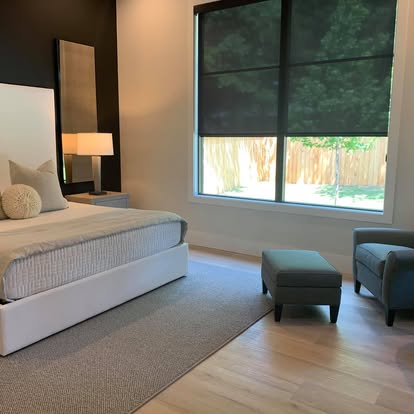 Minimal bedroom with a dark solar roller shade framing a garden view — product style example