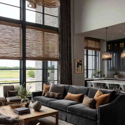 Tall natural woven shades in a two-story great room with charcoal sofa and stone accents